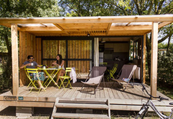 Dos personas relajándose y tomando algo en la terraza de madera del Chalet Evasion en Huttopia Saumur, Francia.