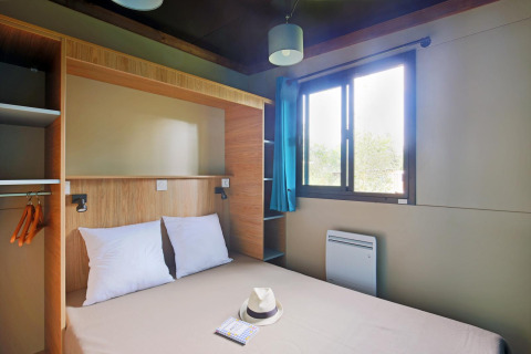 Habitación moderna de glamping en Chalet Evasion con cama doble, ventana, armario y decoración minimalista.