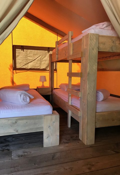 Interior de una tienda safari en Camping Paradis La Bretonnière, Francia, con literas de madera.