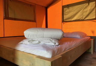 Interieur van een safaritent met houten bed en lakens op Camping Paradis La Bretonniere in Frankrijk.