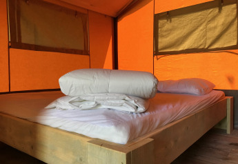 Interior de una tienda safari con cama de madera y ropa de cama en Camping Paradis La Bretonniere, Francia.
