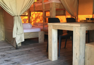 Binnenzicht van een safaritent op Camping Paradis La Bretonniere in Frankrijk met stapelbedden en houten tafel.