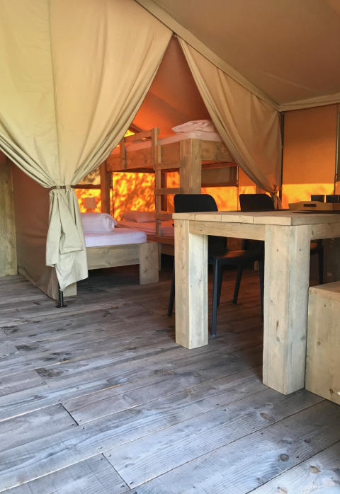 Vista interior de una tienda safari en Camping Paradis La Bretonniere, Francia, con literas y mesa de madera.