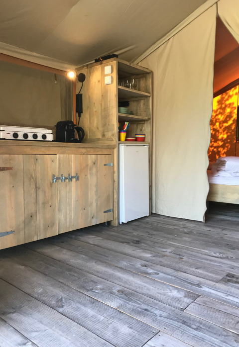 Vista interior de tienda safari en Camping Paradis La Bretonniere, Francia, con cocina y suelo de madera.