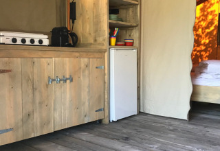 Binnenzicht van safaritent op Camping Paradis La Bretonniere in Frankrijk met kookhoek en houten vloer.