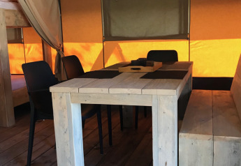 Innenaufnahme eines Safari-Zelts auf Camping Paradis La Bretonniere mit Holzmöbeln und Stühlen.