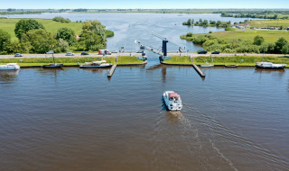 Vista de un canal con un barco, puente y campos verdes cerca de Molkwerum, Frisia, Países Bajos.