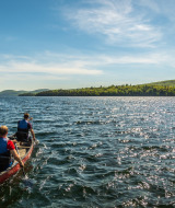 Dos personas reman en una canoa en un lago en un parque vacacional que ofrece alojamiento glamping.