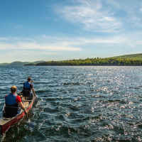 Dos personas reman en una canoa en un lago en un parque vacacional que ofrece alojamiento glamping.
