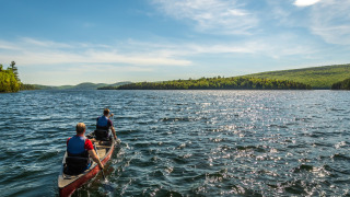Dos personas reman en una canoa en un lago en un parque vacacional que ofrece alojamiento glamping.