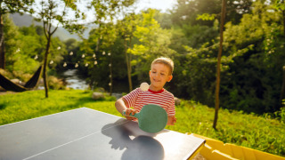 Niño juega tenis de mesa al aire libre, rodeado de naturaleza en Minicamping Marina Warns, Frisia, Países Bajos.