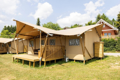 Safaritent Dreamer 49 met houten veranda en overkapping op gras, onder een mooie blauwe lucht gelegen.