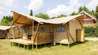 Safari-Zelt namens Dreamer 49 mit überdachter Holzterrasse auf einer Wiese bei schönem Wetter.