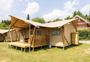 Tenda safari chiamata Dreamer 49 con ampia veranda in legno, situata su prato sotto un cielo blu chiaro.