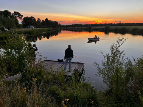 Tramonto sul lago di Camping de Beerte, Groningen, con persone che pescano e una persona in barca.
