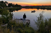 Solnedgang ved søen i Camping de Beerte, Groningen, med folk der fisker og en person i en robåd.