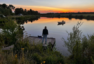 Solnedgang ved søen i Camping de Beerte, Groningen, med folk der fisker og en person i en robåd.