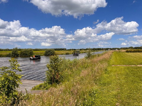 Des bateaux naviguent sur un canal près de Beerta, Groningue, entourés de champs verts et d’un ciel nuageux.