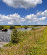 Barcos navegan por un canal junto a Beerta, Groningen, rodeados de vegetación y cielo con nubes blancas.
