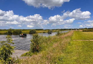 Des bateaux naviguent sur un canal près de Beerta, Groningue, entourés de champs verts et d’un ciel nuageux.