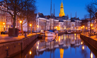 Vista nocturna de un canal con barcos y edificios históricos en Groningen, Países Bajos, iluminado por farolas.