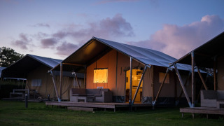 Tenda safari al parco vacanze De Boshoek nei Paesi Bassi al tramonto, con ingresso illuminato.
