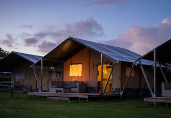 Safaritent bij Vakantiepark De Boshoek in Nederland tijdens zonsondergang met verlichte entree en veranda.