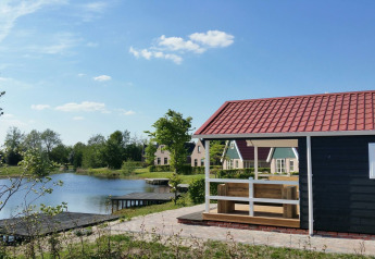 Een houten chalet lodge met rood dak aan het meer in Holiday Park Eigen Wijze, Nederland, op een zonnige dag.