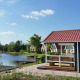 En træhytte med rødt tag ved en sø på Holiday park Eigen Wijze, Nederlandene, under en blå himmel.