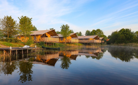 Tiendas glamping cómodas junto al lago en Holiday park Eigen Wijze, Países Bajos, rodeadas de árboles.
