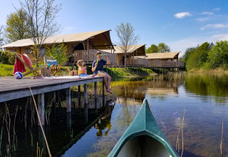 Gezin ontspant op een houten steiger aan het water bij luxe safaritenten in vakantiepark Eigen Wijze.