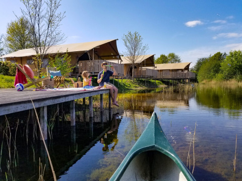 Gezin ontspant op een houten steiger aan het water bij luxe safaritenten in vakantiepark Eigen Wijze.