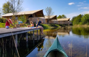 Gezin ontspant op een houten steiger aan het water bij luxe safaritenten in vakantiepark Eigen Wijze.