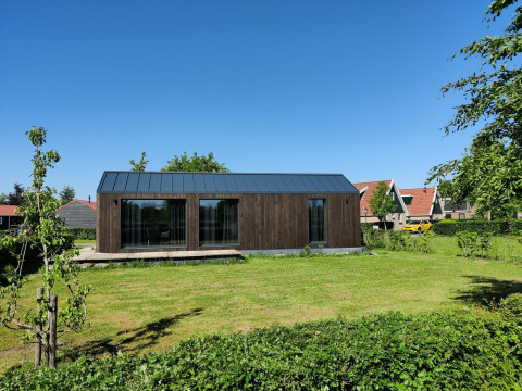 Lille træhus i Holiday park Eigen Wijze i Holland, omgivet af græsplæne og blå himmel.