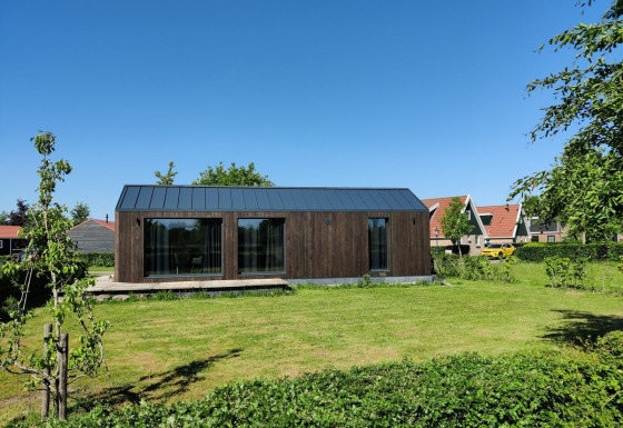 Klein houten huisje op Holiday park Eigen Wijze in Nederland, omringd door gras en een blauwe lucht.