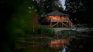 Vista nocturna de una tienda SafariCottage XL iluminada en Holiday Park Sallandshoeve, Países Bajos.