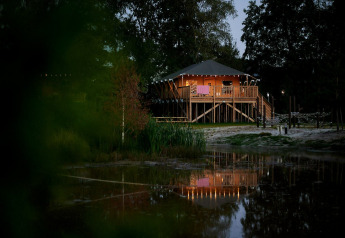 Avondbeeld van een verlichte Safaricottage XL op palen aan het water bij Holiday Park Sallandshoeve.