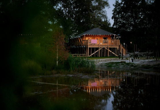 Vista nocturna de una tienda SafariCottage XL iluminada en Holiday Park Sallandshoeve, Países Bajos.