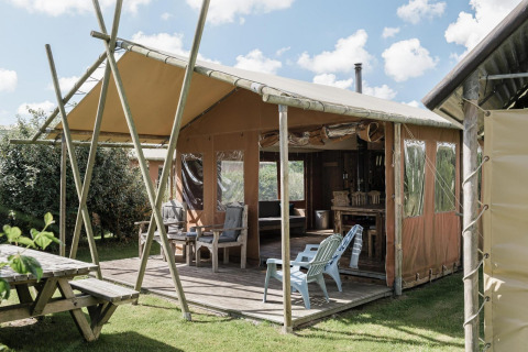 Tienda tipo lodge en Duynpark Het Zwanenwater, Países Bajos, con terraza, sillas y banco de pícnic de madera.