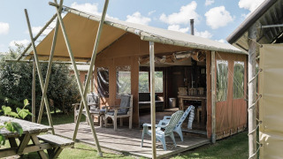 Tienda tipo lodge en Duynpark Het Zwanenwater, Países Bajos, con terraza, sillas y banco de pícnic de madera.