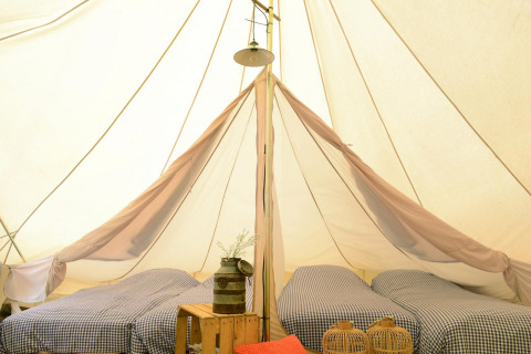 Binnen in Tipitent de Jutter: drie éénpersoonsbedden met ruitjeslakens en rustieke decoratie in de tent.