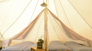 Inside Tipitent de Jutter: Three single beds with checked bedding, rustic decor, and soft light in the tent.