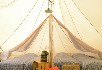 Inside Tipitent de Jutter: Three single beds with checked bedding, rustic decor, and soft light in the tent.