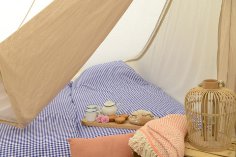 Interior de una Tipitent de Jutter con ropa de cama a cuadros azules, tetera, tazas y decoración acogedora.