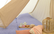 Interior de una Tipitent de Jutter con ropa de cama a cuadros azules, tetera, tazas y decoración acogedora.
