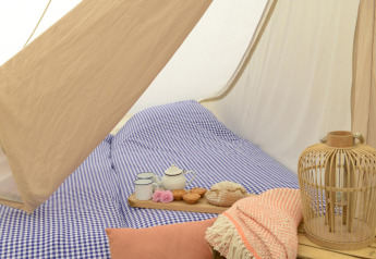 Intérieur d’une Tipitent de Jutter avec linge de lit à carreaux bleus, théière, mugs et décoration chaleureuse.