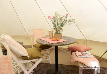 Cozy interior of Tipitent de Jutter at Duynpark Het Zwanenwater with chairs, table, pillows, and fresh flowers.