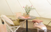 Intérieur douillet du Tipitent de Jutter à Duynpark Het Zwanenwater avec table, chaises, coussins et fleurs.