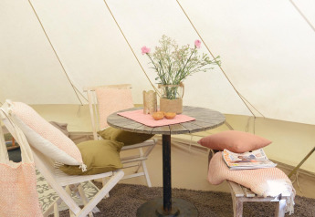 Interior acogedor del Tipitent de Jutter en Duynpark Het Zwanenwater con mesa, sillas, cojines y flores.