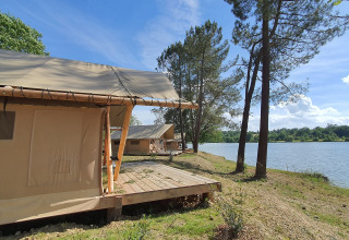 Safari tents by the lakeside under a blue sky at Huttopia Lac de l'Uby - Gers, France.